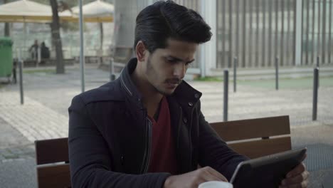 Serious-young-man-using-tablet-computer-on-street